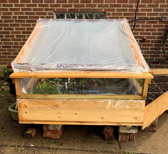 A raised cold frame built with wood and plastic